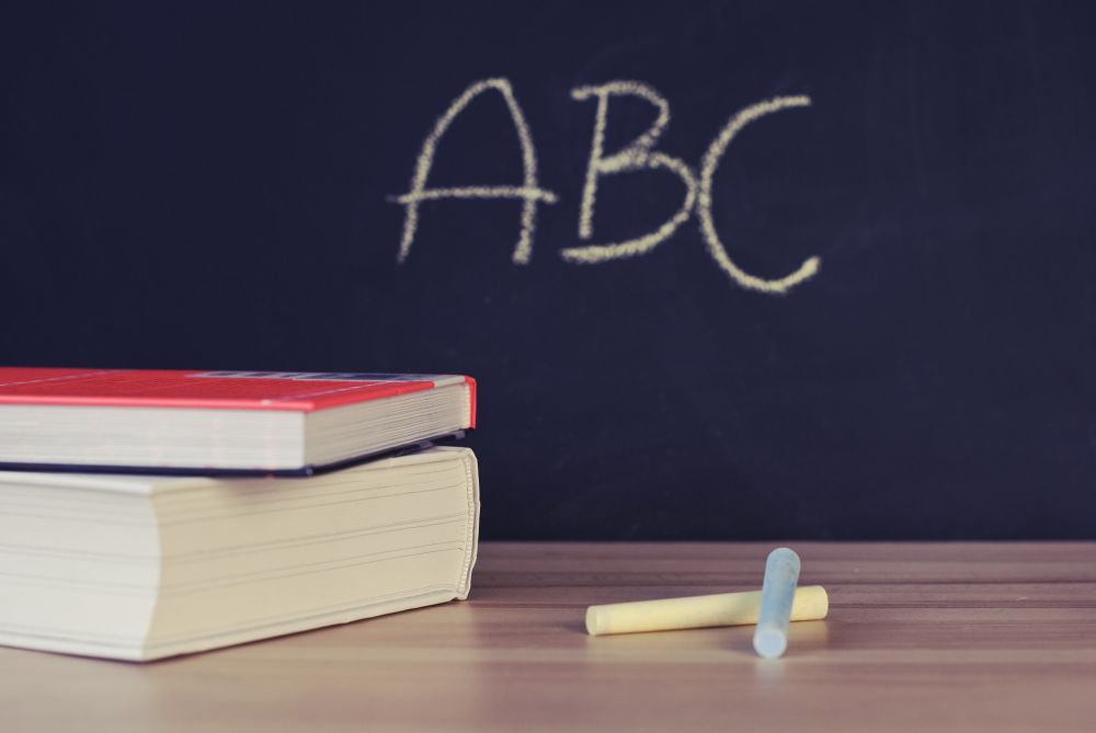 Bücher liegen auf dem Tisch, im Hintergrund eine Tafel auf der ABC steht.