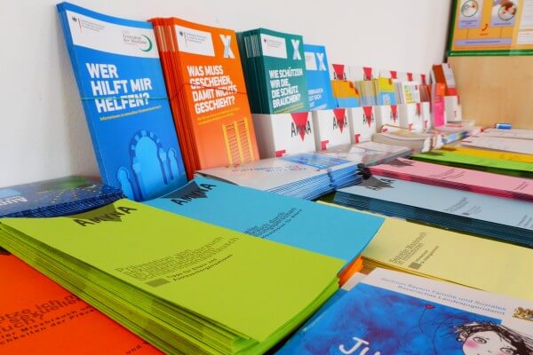 Auf einem Tisch liegen einige Stapel an Broschüren und Mappen.